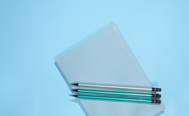 Blue notepad and wooden pencils on a blue background, top view