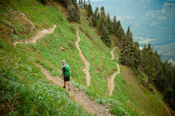 A backpacker hikes along the Sauk Mountain Trail as it switches back and forth through a steep alpine meadow.