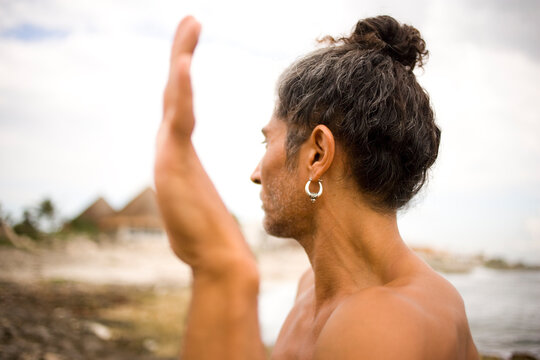 A man practices yoga at a rocky beach on a clear day.