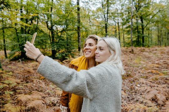 Two blondie women taking a selfie in a autumnal forest