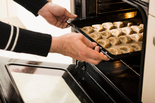 Close-up of a man putting baking tray of vanilla crescents in oven for baking, Munich, Bavaria, Germany