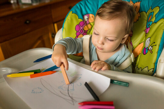 Small boy sitting in high chair and learning how to draw with cr