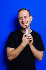 Portrait of a young handsome man brushing his teeth with an ultrasonic modern toothbrush. Oral care. Morning self care