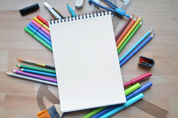 Regreso a clases / Set de útiles escolares: cuaderno, lápices, acuarelas, reglas, colores, block de hojas en blanco sobre escritorio de madera visto desde arriba.
