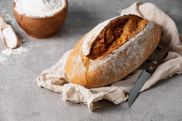 Artisan sourdough wheat bread and a bowl of flour on towel, stone kitchen table. 