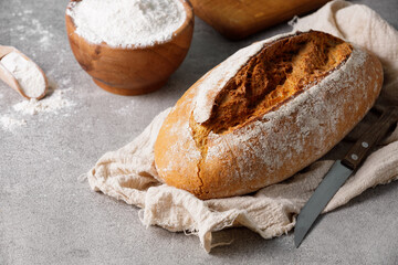 Artisan sourdough wheat bread on towel and bowl with wheat flour, stone kitchen table.