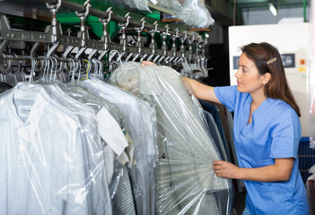 Adult female worker of laundry inspecting clothing after dry cleaning on racks