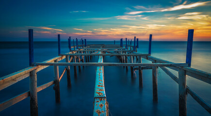 view of wodden pier on blue sea side with sunset colors and clouds at horizon