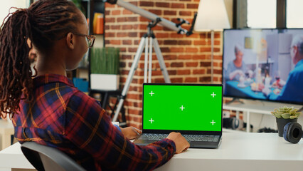 Female employee looking at greenscreen display on laptop, using isolated blank mock up template on...