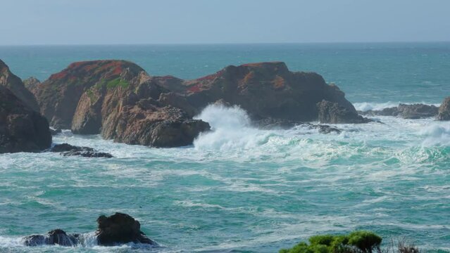 Large waves crashing against rocky island on Big Sur Coastline in Garrapata, cliffs covered in red iceplant in Slow Motion.
