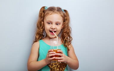 Funny emotion kid girl drinking juice from grass through the straw and looking excited on blue studio background. Closeup