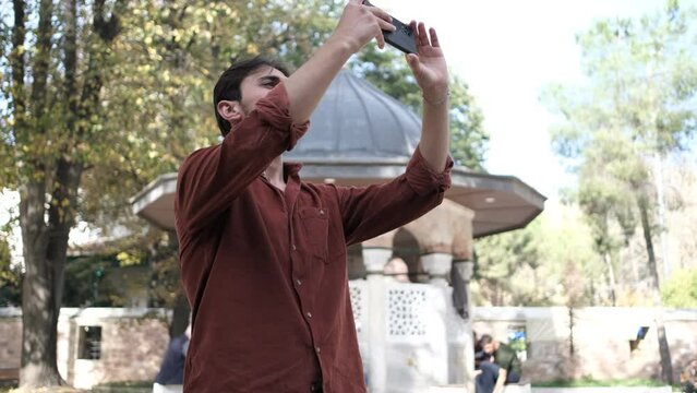 Young bearded man taking pictures with a phone in the garden of the mosque, the mosque is the place where Muslims pray