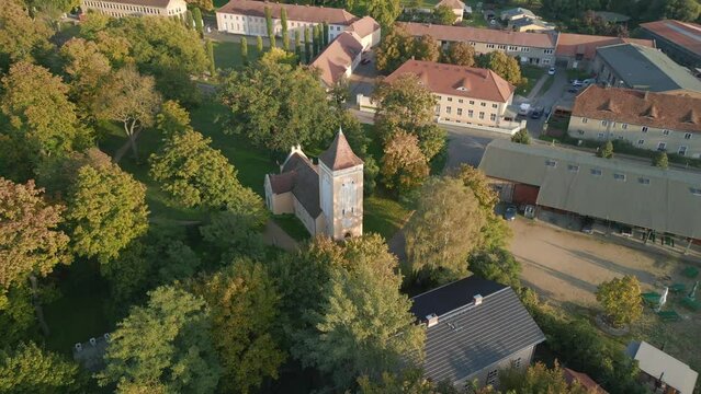 Fairy tale village church in forest park. Magic aerial view flight panorama curved drone
in Paretz Brandenburg Havelland Germany, summer evening 2022. High Quality 4k Cinematic footage