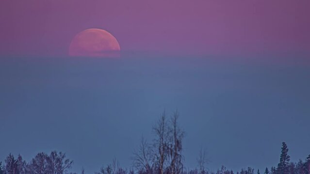 Time lapse of pink moon descending and disappearing behind clouds of colorful sky 