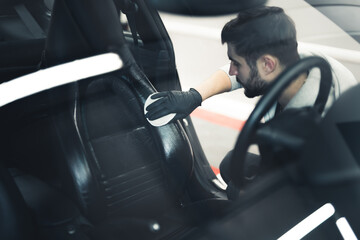 White man wearing black gloves putting protective coating on car seat. Waterproofing leather...