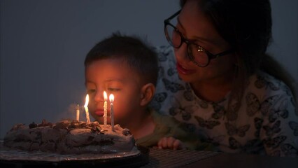 Young little latin baby boy blowing candles on a cake at night with his mom celebrating his birthday