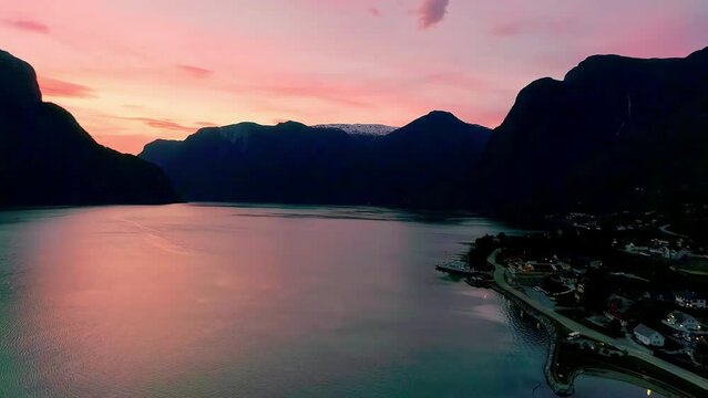 Stunning aerial shot of golden hour pink light that reflects in the lake and black silhouettes of the mountains in buhe background of a norwegian village