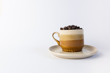 Toned brown cup with coffee beans inside. Front view and a white space on the left