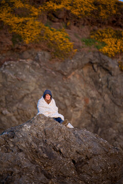 A young woman sists on a rock bluff at Bandon Bay, Oregon.