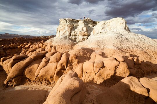 Hikers stand on the summit of a high mesa overlooking the vast field of hoodoos at Goblin Valley State Park, Utah.