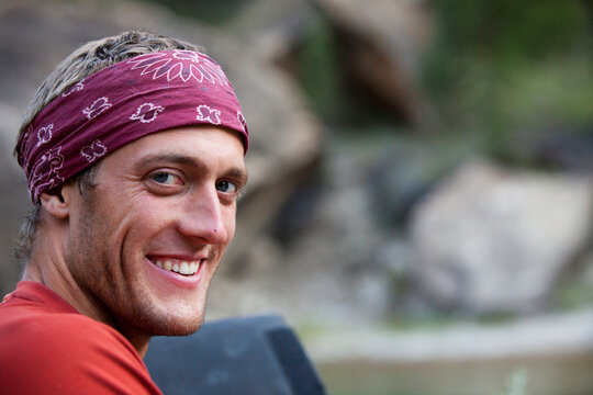 A portrait of a man smiling while looking into the camera with a bandanna on.