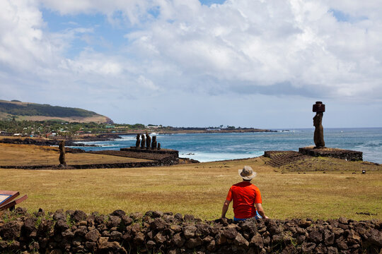 A man in red sits on a rock wall overlooking the Moi and the blue water of the Pacific off the coast of the world's most remote island.