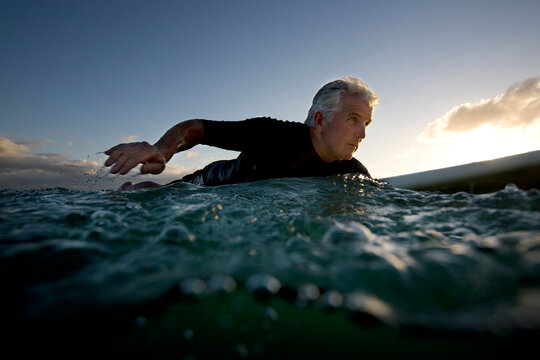 a senior surfer paddles on his surfboard