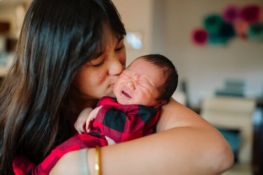 Happy Mom Kissing Her Crying Newborn Baby On His Head