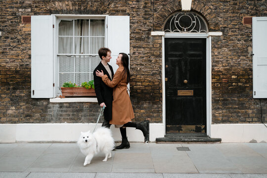 Couple with their dog embracing in front of their house