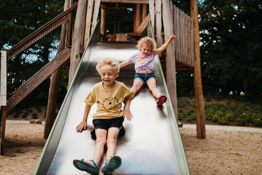 Blond siblings going down a slide at the playground