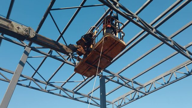 Construction workers on high cherry-picker welding the metal frames on construction site