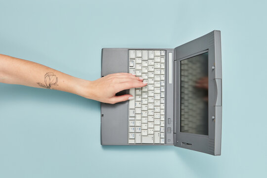 Old 90s laptop with woman's hand pressing key.