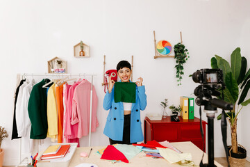 Cheerful female designer recording video in studio with clothes