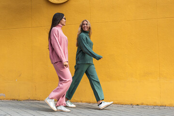 Women friends strolling the city against yellow wall
