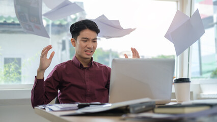 Irritated businessman sitting at office desk throwing up papers with frustrated facial expression. Negative human emotions