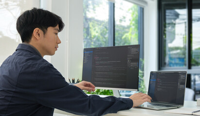 Asian male programmer typing data code on laptop and programming on computer in office.