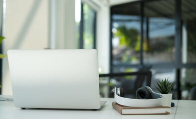 Stylish workplace with laptop, computer, wireless headphone and books on white table.