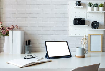 Creative workspace with digital tablet, books, coffee cup and stationery on white desk.