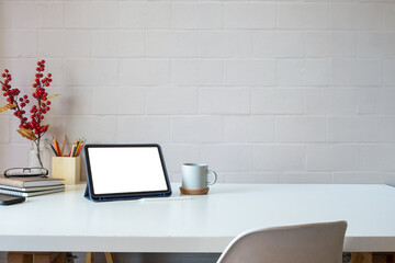 Minimal workspace with digital tablet, books, coffee cup and stationery on white desk against brick wall.