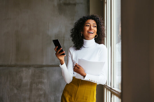 Smiling Woman With Documents And Phone In Office