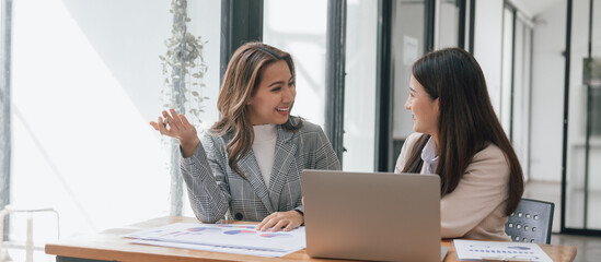 Two young pretty asia business woman in suit talking together in modern office workplace, Thai...
