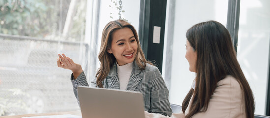 Two young pretty asia business woman in suit talking together in modern office workplace, Thai woman, southeast asian, face to face, talking