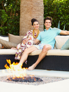 Couple enjoying relaxing in their backyard on sofa with fire pit