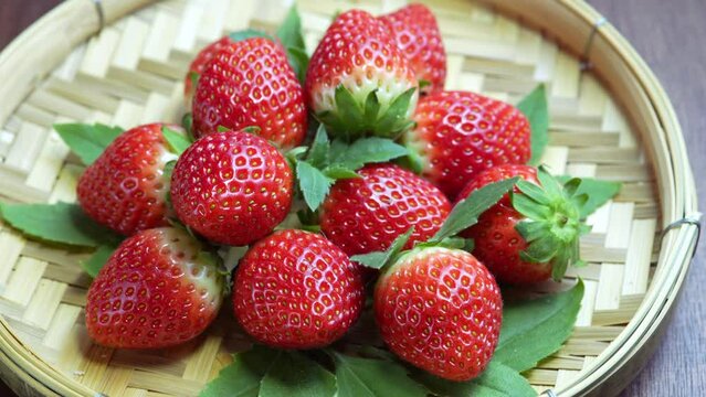Fresh strawberries in a white plate on bamboo basket,  Red strawberries Pine berry or Hula strawberry on wooden background.