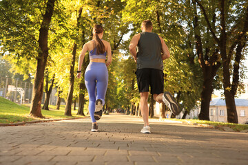 Sporty couple jogging in beautiful park on sunny day, back view