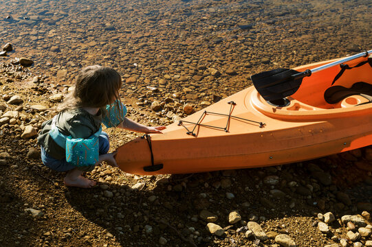 little toddler wearing floatation device by the kayak in the lake