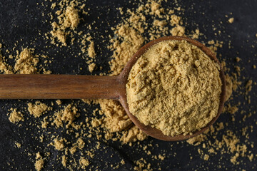 Wooden spoon of aromatic mustard powder on black table, top view