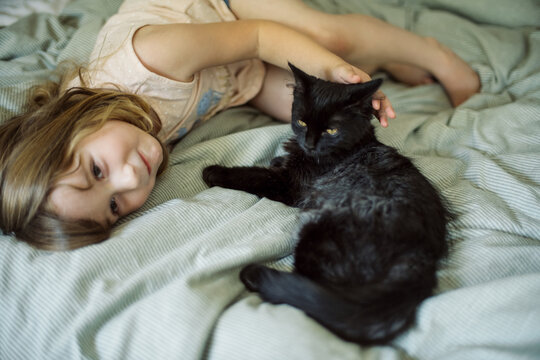 Little girl with her black kitten on a bed