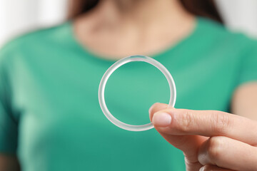 Woman holding diaphragm vaginal contraceptive ring on blurred background, closeup