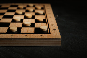 Wooden checkerboard with game pieces on black table, closeup
